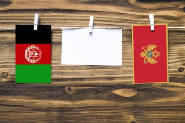 Hanging flags of Afghanistan and Montenegro attached to rope with clothes pins with copy space on white note paper on wooden background.Diplomatic relations between countries. Cooperation concept.