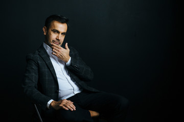 Portrait of a mature, stylish man sitting on chair with finger on chin, in studio 