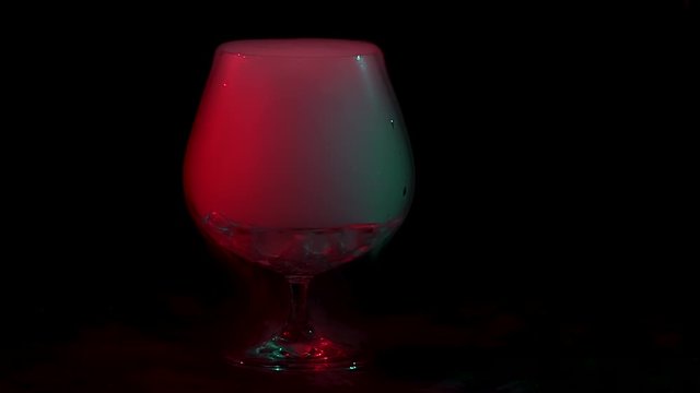 Dry ice bubbling in a cognac glass with smoke on a black background with red light. Slow motion