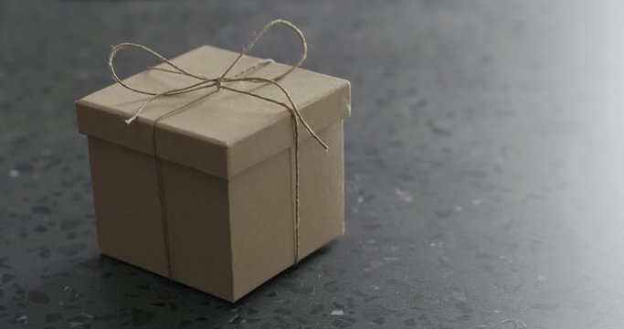 Slow motion man hand unties brown paper gift box on terrazzo countertop