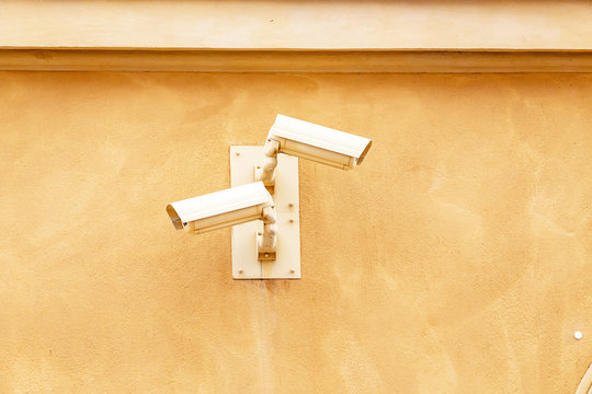 Two cctv security camers on a yellow wall. Privacy and identification concept
