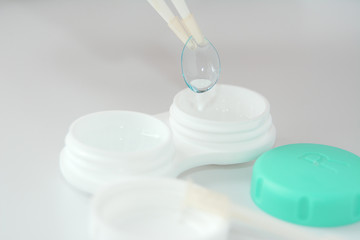 container for soft contact lenses and lens with tweezers on light background