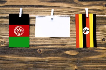 Hanging flags of Afghanistan and Uganda attached to rope with clothes pins with copy space on white note paper on wooden background.Diplomatic relations between countries. Cooperation concept.