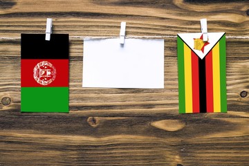 Hanging flags of Afghanistan and Zimbabwe attached to rope with clothes pins with copy space on white note paper on wooden background.Diplomatic relations between countries. Cooperation concept.