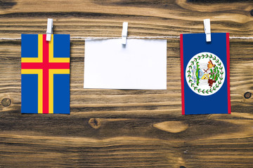 Hanging flags of Aland Islands and Belize attached to rope with clothes pins with copy space on white note paper on wooden background.Diplomatic relations between countries.