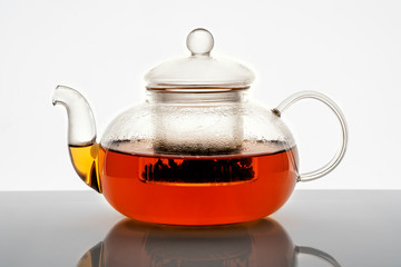 glass teapot with hot tea on white background with reflection
