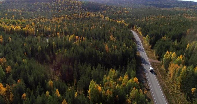 Camper van in a autumn color forest, Aerial, drone shot, of a rv,, driving towards Luosto, in middle of arctic foliage, on a sunny, ruska season day, in Pyha-Luosto national park, Sodankyla, Finland