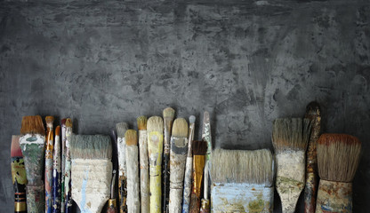 row of old artist paintbrushes on a dark gray decorative stucco surface