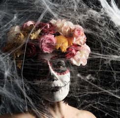 girl with black hair is dressed in a wreath of multi-colored roses and makeup is made on her face Sugar skull to the day of the Dead