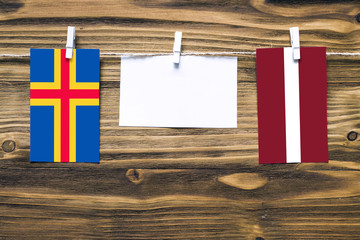 Hanging flags of Aland Islands and Latvia attached to rope with clothes pins with copy space on white note paper on wooden background.Diplomatic relations between countries.