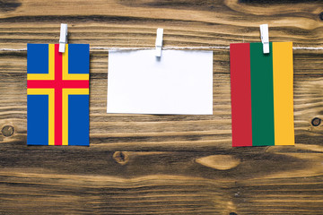 Hanging flags of Aland Islands and Lithuania attached to rope with clothes pins with copy space on white note paper on wooden background.Diplomatic relations between countries.