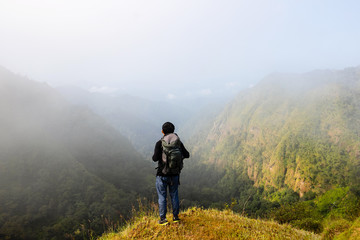 Fototapeta premium A backpack man standing on cliff and see over view in nature.Tourist enjoying fresh air. A man enjoying free happiness in beautiful Thailand landscape.
