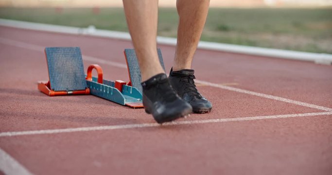 Low angle shot of an athlete putting feet on starting blocks on stadium track, blasting off and having a quick start - sports concept 4k footage