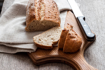 Loaf of whole wheat bread with slices on wooden board on kitchen table