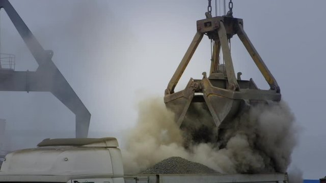 Grapple crane unloading cement clinker from ship to truck in river port. Barge delivery of dusty bulk cargo. Gantry crane unloading and loading in Harbor, outdoors. Logistics. Commerce, nautical