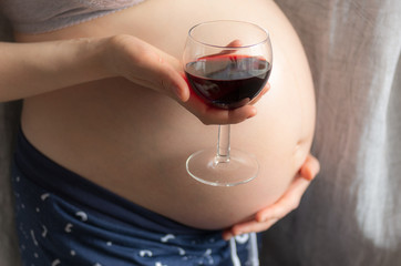 pregnant woman holding a glass of wine on background of the pregnant belly, the concept of alcohol intake during pregnancy