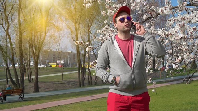 Man in sunglasses talks on smartphone in the park. Man in red baseball cap with smartphone