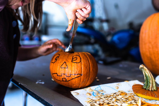 Young Girl Working On Carving A Small Pumpkin With Seeds All Around