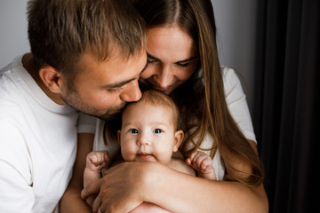 Young beautiful happy parents holding cute little baby and kissing her head