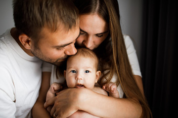 Young beautiful happy parents holding cute little baby and kissing her head