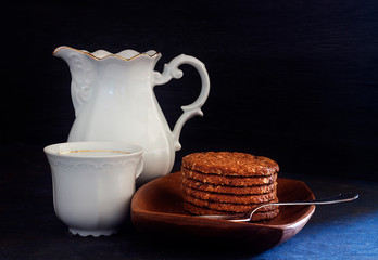 BREAKFAST WITH CHOCOLATE COOKIES IN WOOD PLATE NEXT TO CUP AND COFFEE JUG ON DARK FUND