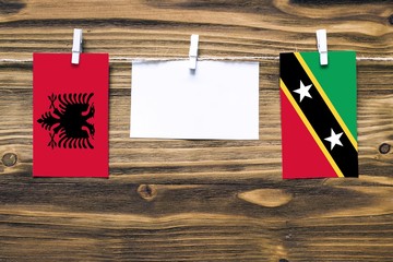 Hanging flags of Albania and Saint Kitts And Nevis attached to rope with clothes pins with copy space on white note paper on wooden background.Diplomatic relations between countries.