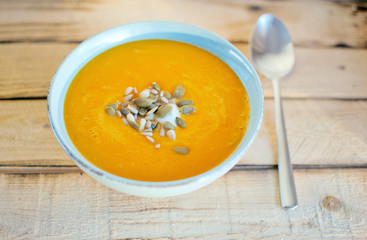 Blue bowl with homemade pumpkin cream soup flavored with yogurt and seeds on rustic wooden table