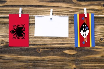 Hanging flags of Albania and Swaziland attached to rope with clothes pins with copy space on white note paper on wooden background.Diplomatic relations between countries.