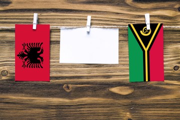 Hanging flags of Albania and Vanuatu attached to rope with clothes pins with copy space on white note paper on wooden background.Diplomatic relations between countries.