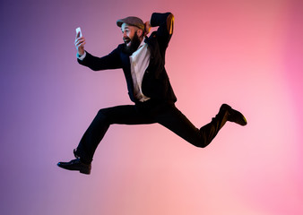 Full length portrait of happy jumping man wearing office clothes in neon light isolated on gradient...