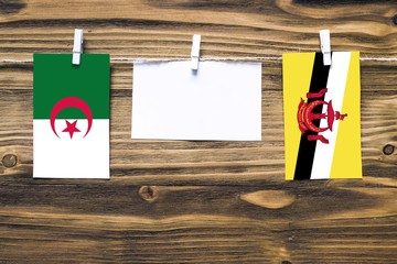 Hanging flags of Algeria and Brunei attached to rope with clothes pins with copy space on white...