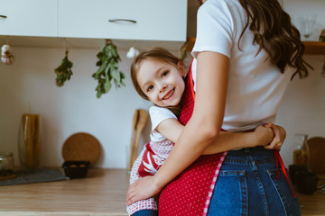 daughter hugs mom at the waist in the kitchen
