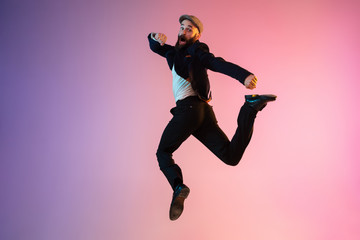 Full length portrait of happy jumping man wearing office clothes in neon light isolated on gradient background. Emotions, ad concept. Calling, hurrying up, office work or sale, shopping. Copyspace.