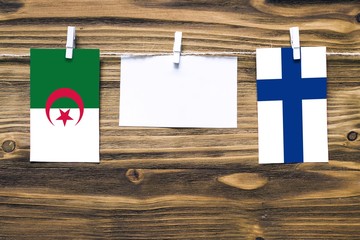 Hanging flags of Algeria and Finland attached to rope with clothes pins with copy space on white note paper on wooden background.Diplomatic relations between countries.