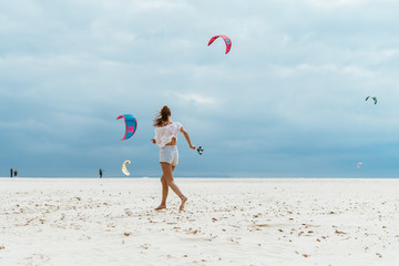 girl runs along the beach on the background of flying skites