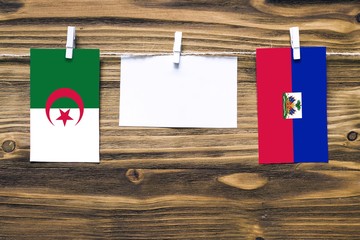 Hanging flags of Algeria and Haiti attached to rope with clothes pins with copy space on white note paper on wooden background.Diplomatic relations between countries.