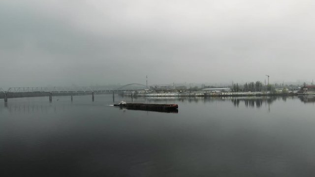 Iron barge sailing on empty calm river through industrial smog at downtown. Big scow floating through bridge in downtown in fog, aerial drone shot