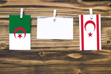 Hanging flags of Algeria and Northern Cyprus attached to rope with clothes pins with copy space on white note paper on wooden background.Diplomatic relations between countries.