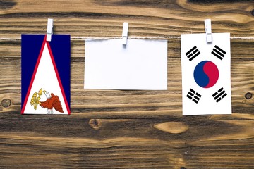 Hanging flags of American Samoa and South Korea attached to rope with clothes pins with copy space on white note paper on wooden background.Diplomatic relations between countries.