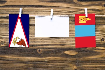 Hanging flags of American Samoa and Mongolia attached to rope with clothes pins with copy space on white note paper on wooden background.Diplomatic relations between countries.