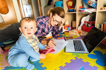 baby looking at camera while his mother works on the computer, concept of woman's work-life balance.