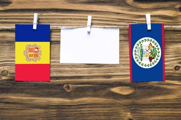 Hanging flags of Andorra and Belize attached to rope with clothes pins with copy space on white note paper on wooden background.Diplomatic relations between countries.