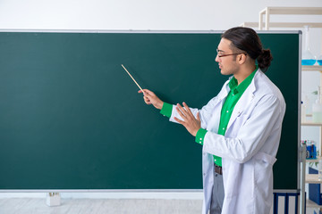Young male chemist teacher in front of blackboard