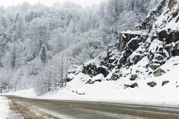 Snowy road scene in winter, with snowy trees, rocks and asphalt road.