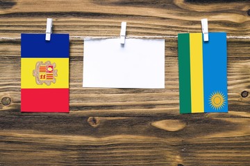 Hanging flags of Andorra and Rwanda attached to rope with clothes pins with copy space on white note paper on wooden background.Diplomatic relations between countries.