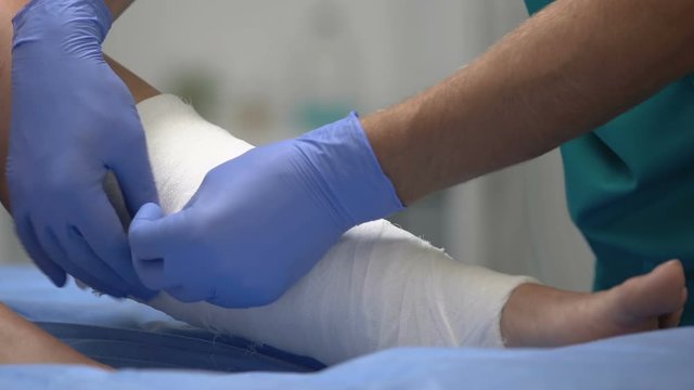 Doctor putting roller bandage on patient leg, medical treatment in hospital