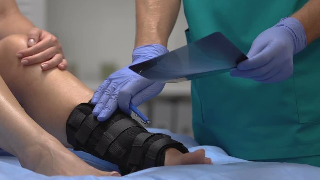 Traumatologist explaining x-ray results to patient with ankle wrap, health care