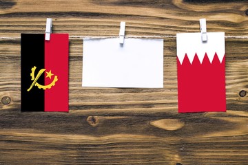 Hanging flags of Angola and Bahrain attached to rope with clothes pins with copy space on white...