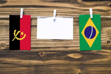 Hanging flags of Angola and Brazil attached to rope with clothes pins with copy space on white note...