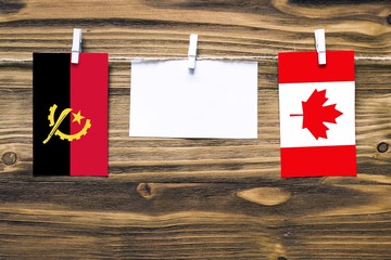 Hanging flags of Angola and Canada attached to rope with clothes pins with copy space on white note...